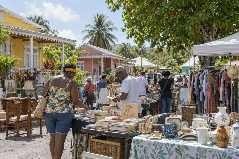 Vide-greniers illustratif avec stands et végétation tropicale dans un décor antillais